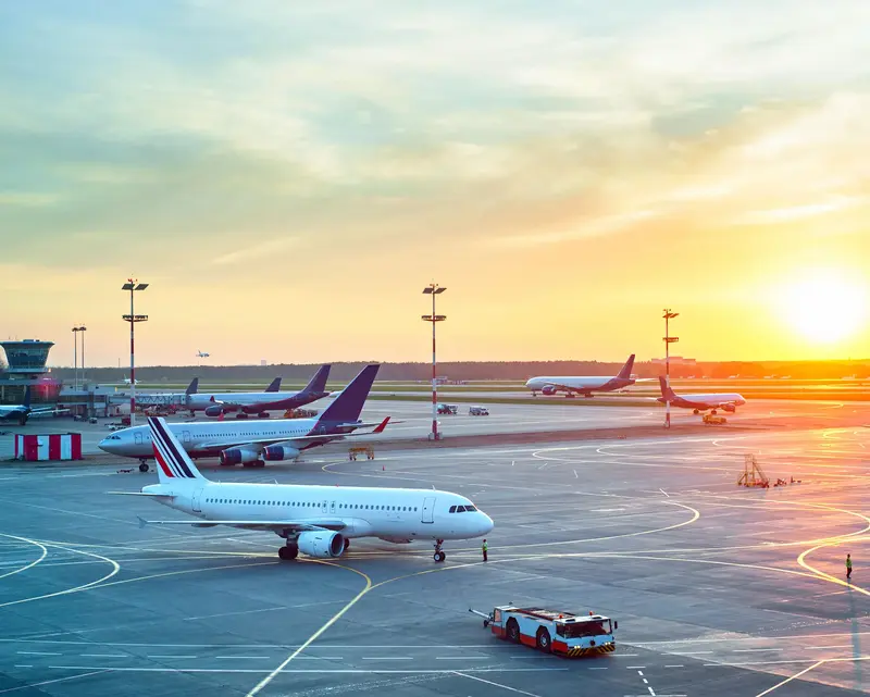 Commercial airplanes on apron at dusk with vibrant sunset sky at a busy airport.