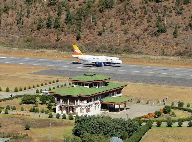 Commercial plane on runway at Paro Airport beside Bhutanese-style building.