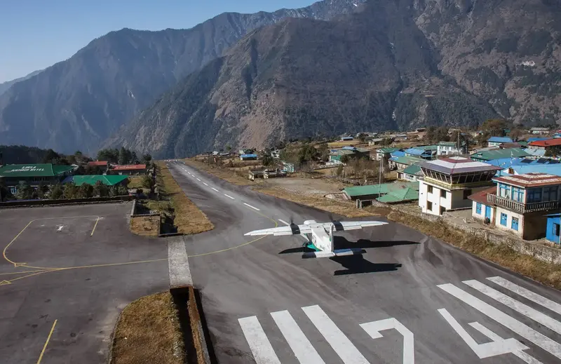 Small plane poised on the steep runway of Tenzing-Hillary Airport, with Himalayan backdrop.