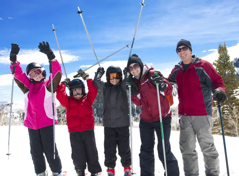 A happy family with ski gear raising their poles in triumph on a sunny Snowbird, Utah mountain.