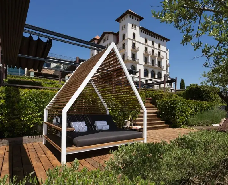 A modern outdoor lounger in the lush gardens of Gran Hotel La Florida with the hotel in the background.