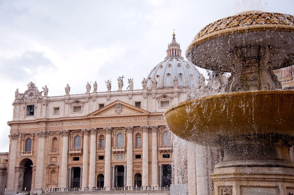 Photograph of St. Peter's Basilica in Vatican City, showcasing its imposing architecture with a detailed facade, large dome, and a clear blue sky in the background. The basilica stands as a significant landmark for visitors exploring Vatican City.
