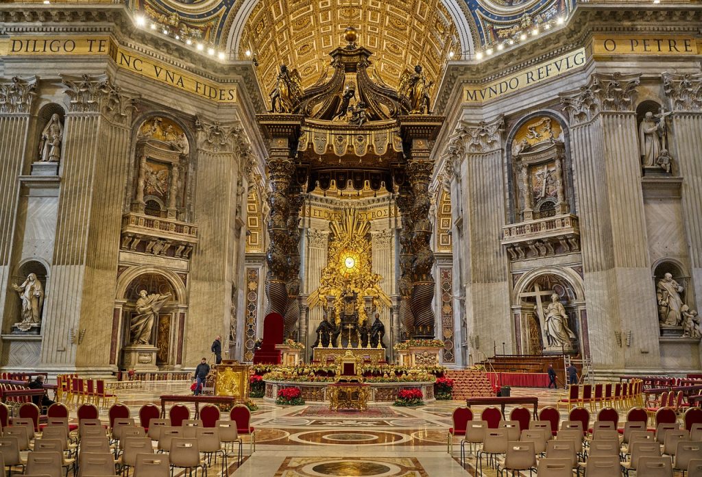 Interior view of St. Peter's Basilica in Vatican City, with its grand altar, ornate golden details, and majestic columns. The intricate floor patterns lead to the central nave, surrounded by impressive sculptures and artwork, embodying the site's historical and religious significance.