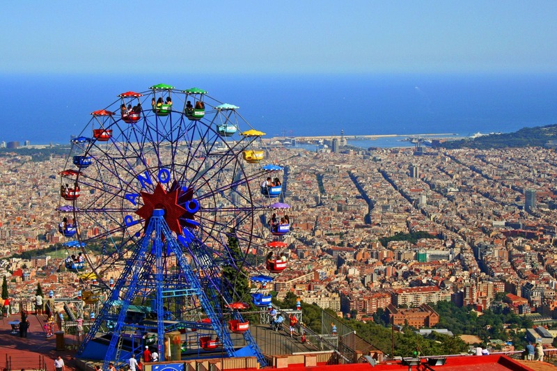Colorful Ferris wheel at Tibidabo Amusement Park providing panoramic views of Barcelona's sprawling cityscape, with the Mediterranean Sea in the horizon, capturing the essence of fun and sightseeing combined in one of the city's highest vantage points.