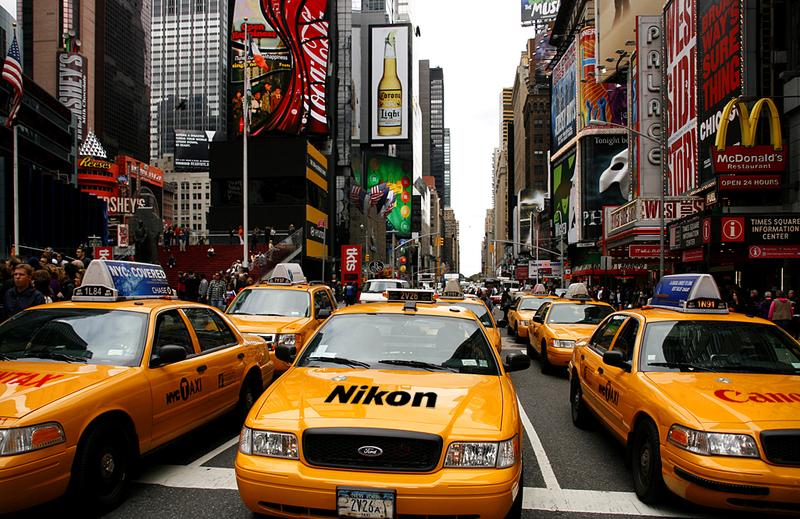 Yellow taxis lined up in Times Square, New York City, with crowded sidewalks and vibrant billboards, illustrating the busy urban life for visitors getting to know the city.
