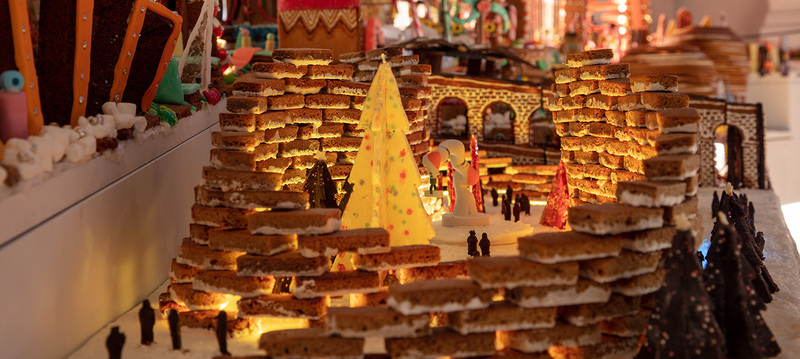 A detailed gingerbread village display featuring a lighted Christmas tree centerpiece, showcasing the creative and edible artistry that’s part of the Christmas things to do in New York
