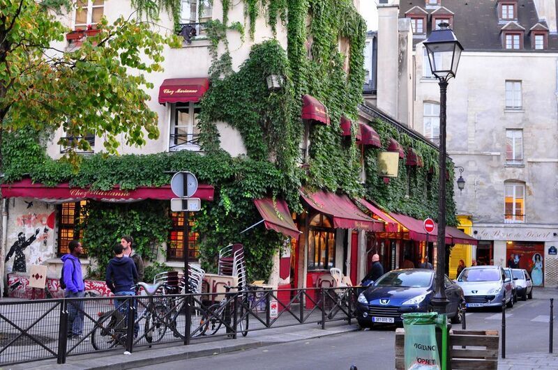 Image of a quaint cafe covered in green ivy, with locals and visitors mingling in the Marais district of Paris, capturing the essence of city life for travelers on a short itinerary.