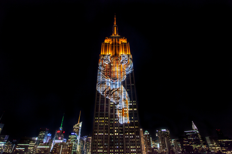 A striking projection on the Empire State Building at night, with the cityscape of New York lit up in the background, highlighting the innovative Christmas things to do in New York.