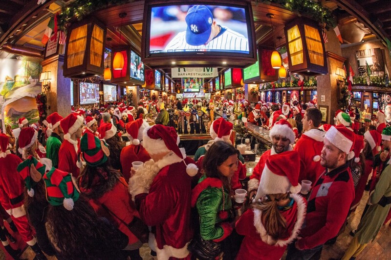 A crowded bar in New York City teems with festive party-goers in Santa outfits during SantaCon, embodying the spirited and unconventional Christmas things to do in New York.