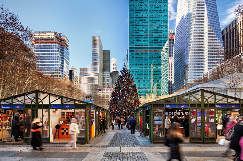 Bustling Winter Village in Bryant Park with a large, decorated Christmas tree in the background, surrounded by holiday shops and visitors, capturing the essence of Christmas things to do in New York.