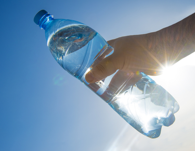 Hand holding a clear bottle of water up to the sunlight, a practical tip for visitors to stay hydrated while exploring New York City.