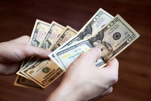 Hands counting various US dollar bills, a reminder for travelers about the importance of carrying cash when visiting New York City for small purchases and tips