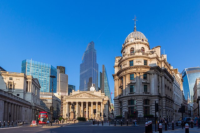 The contrasting architectural styles of the City of London with the classical Royal Exchange building in the foreground, flanked by modern glass skyscrapers, and a red double-decker bus adding a pop of color to the scene.