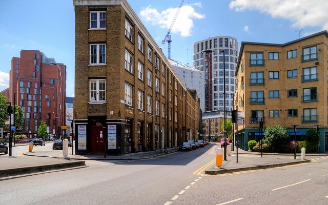 A quiet street in Hackney, London, on a sunny day, featuring a blend of classic brick buildings and modern architectural developments.