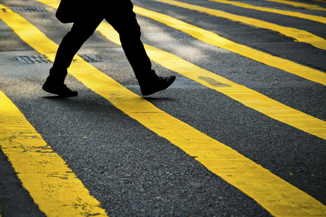 Close-up of a person's legs crossing a street in New York City, walking over a crosswalk with bright yellow stripes, highlighting the importance of pedestrian safety in the bustling city.