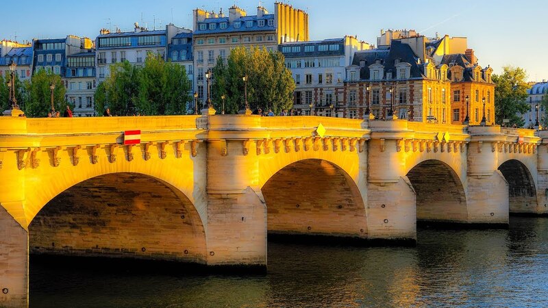 The historic Pont Neuf bridge bathed in the golden light of sunset, with its stone arches casting reflections on the Seine River. Classic Parisian buildings in warm hues line the backdrop, while the evening's soft light highlights the bridge's elegant structure and the serene waters below.