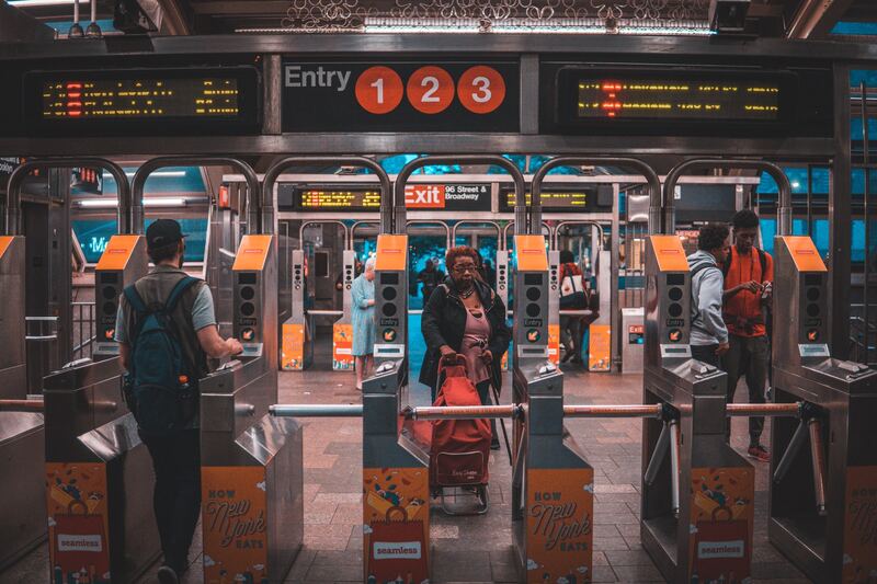 Commuters passing through turnstile gates at a New York City subway station, an essential experience for visitors familiarizing themselves with public transportation in the city.