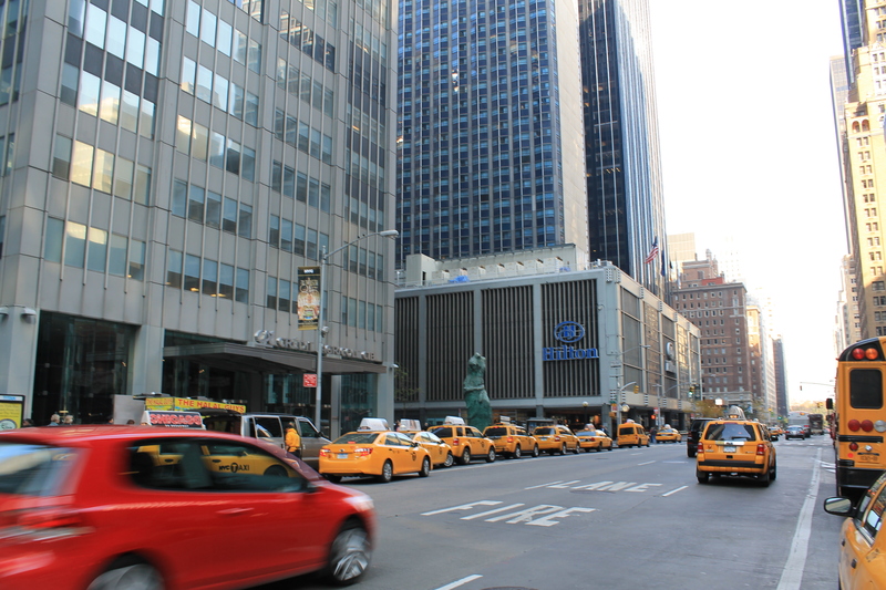 A typical New York scene with a stream of yellow taxis on Sixth Avenue, set against a backdrop of towering buildings, capturing the city's dynamic atmosphere as part of the Christmas things to do in New York.