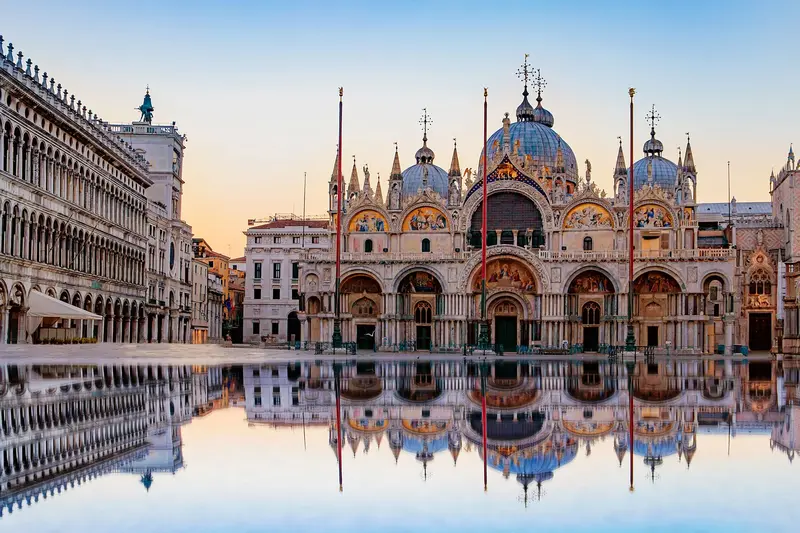 Sunrise at St. Mark's Basilica in Venice with a clear reflection on water.
