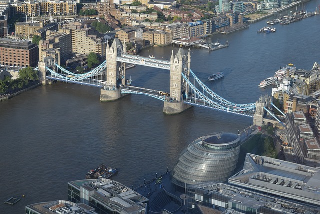 An aerial view of the Thames River winding through London, with the majestic Tower Bridge prominently displayed, surrounded by the modern architecture of the cityscape. 