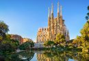 The La Sagrada Família basilica in Barcelona, captured on a clear day, with its intricate Gothic and Art Nouveau façades and towering spires reflecting in the pond in front, surrounded by lush greenery.
