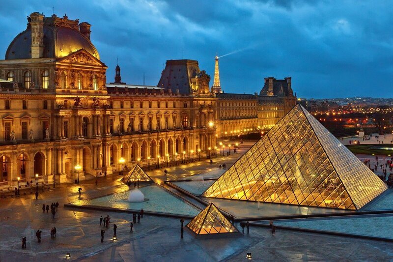The Louvre Pyramid lit up at dusk with the Eiffel Tower in the background.